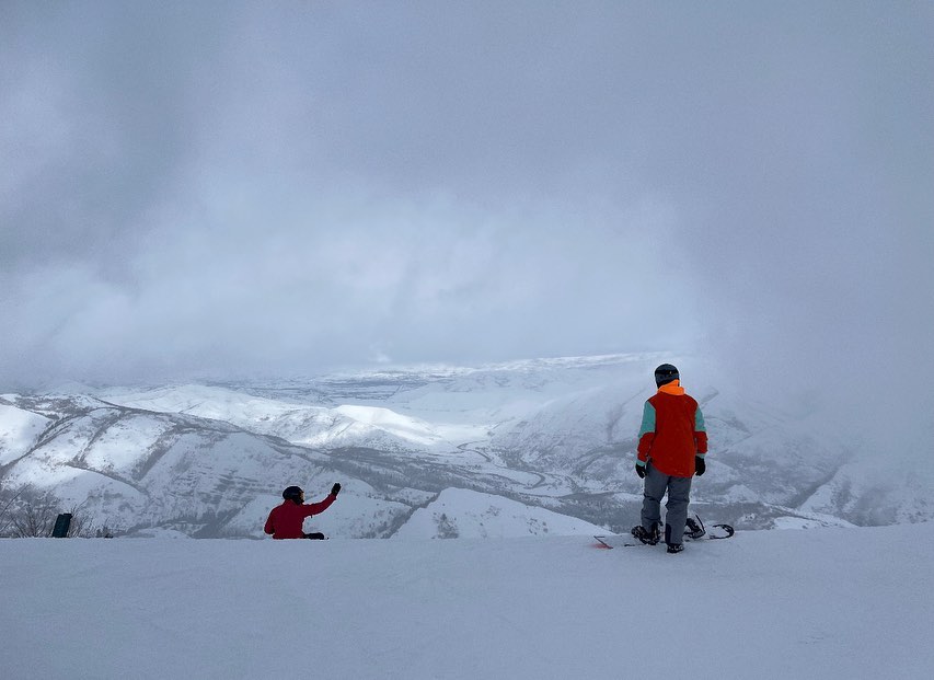 A snowboarder looking over a snowy ridge.